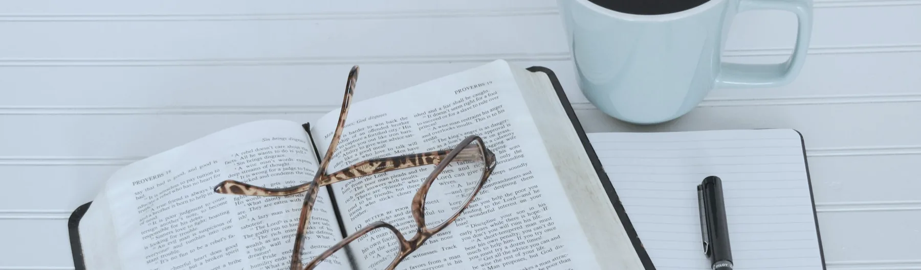 Unbedruckte Tasse, Notizblock, Kugelschreiber und Brille auf einem Tisch